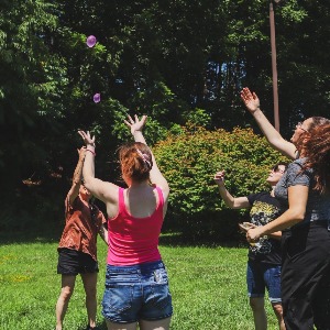 a group of people outside in the sun reaching up to try and catch water balloons