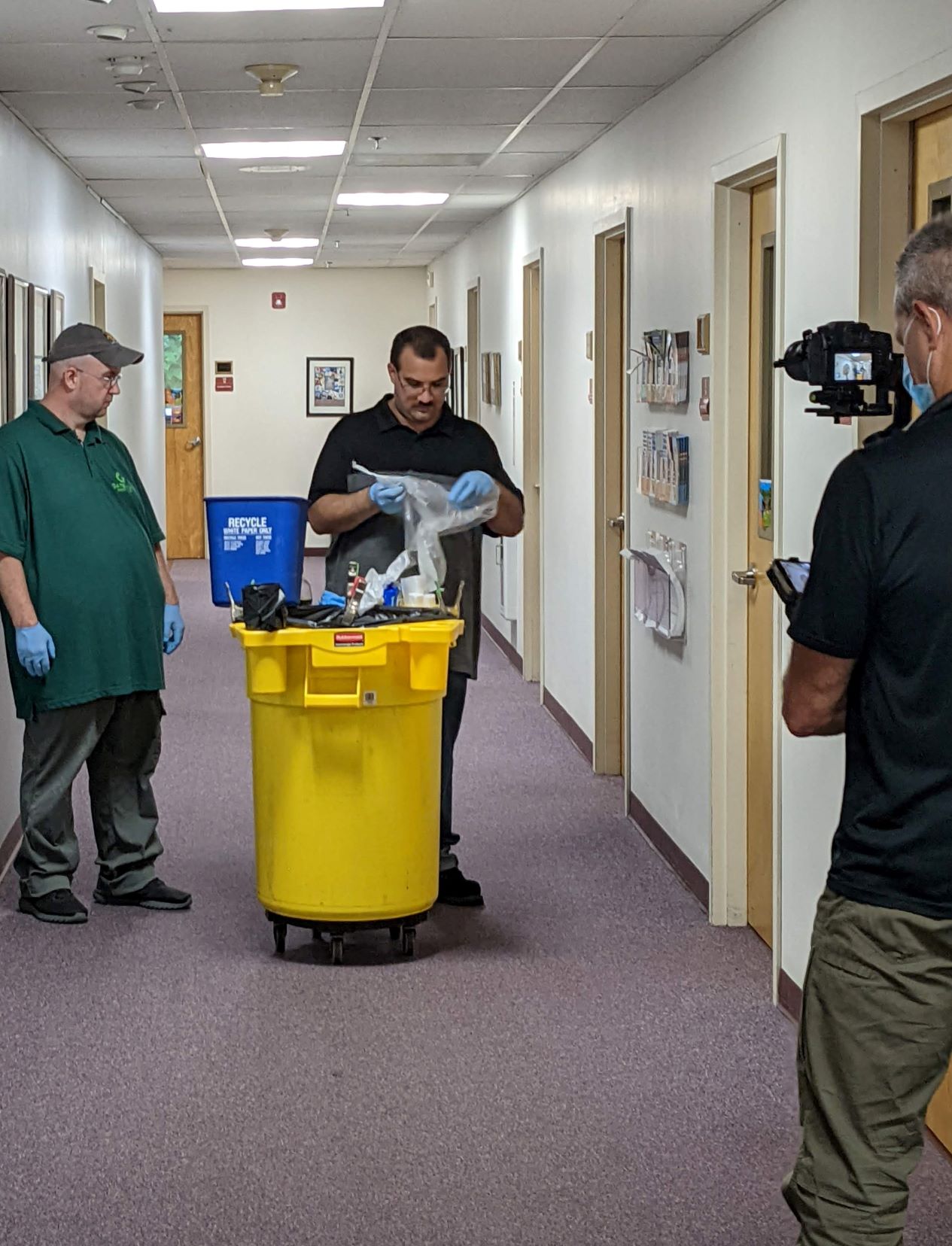 Videographer filming two janitors in an office hallway
