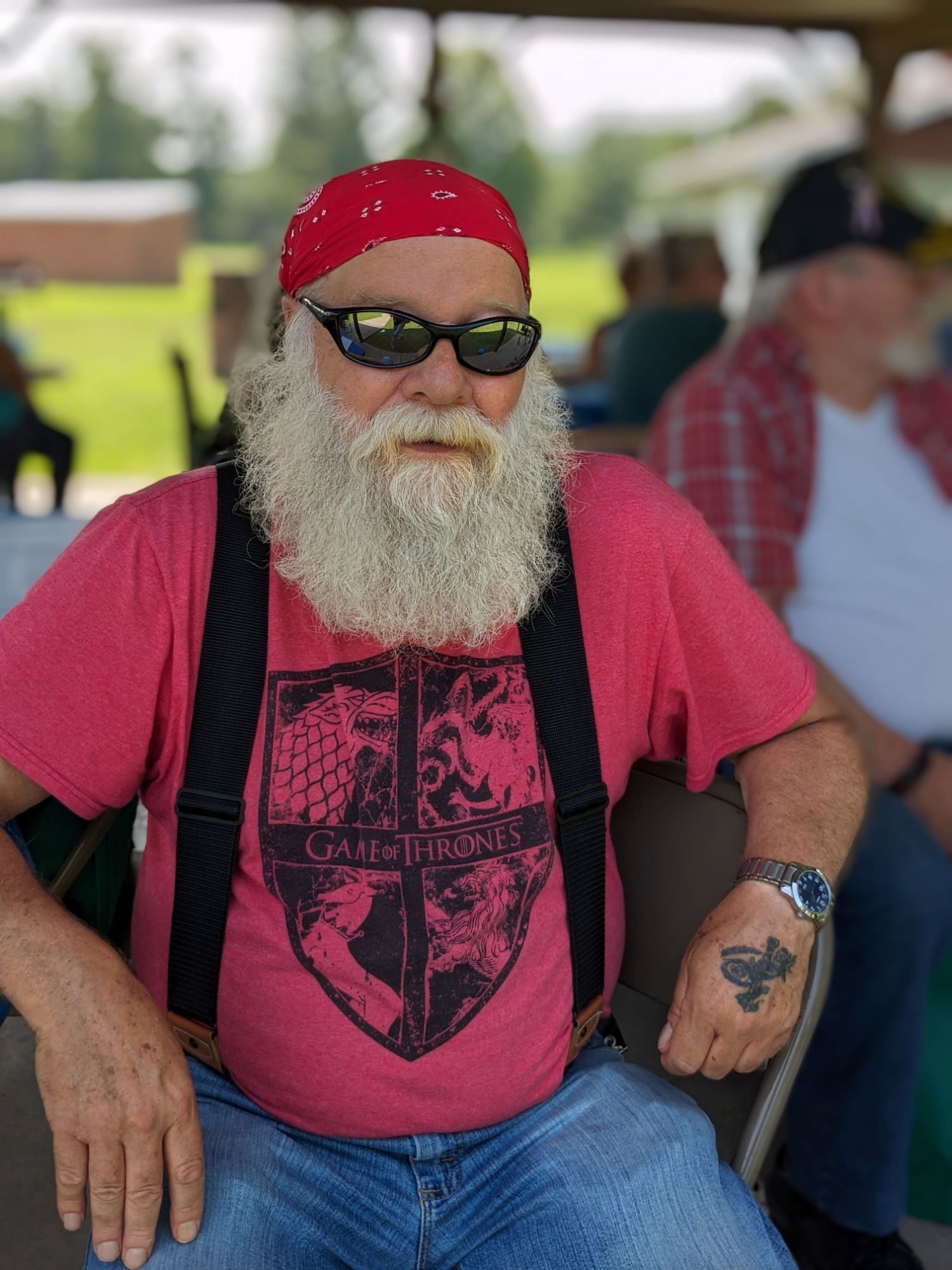 white bearded man with red bandana on his head and red tee shirt with black suspenders.