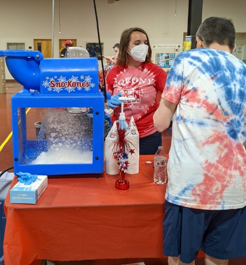Woman in red shirt serving a man in a tie-dye shirt a snow cone