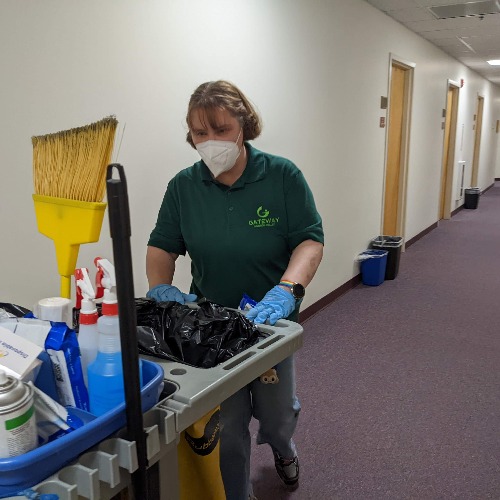 Female employee pushing a cleaning cart down an office hallway