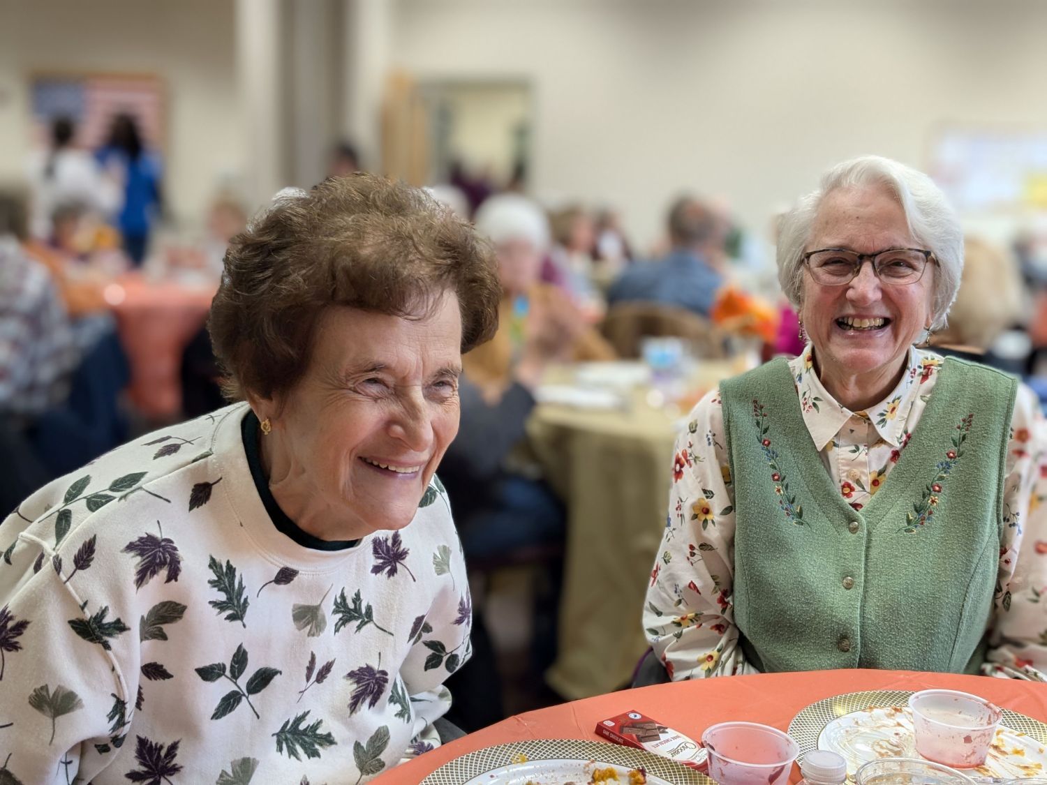 two women laughing while sitting at a lunch table