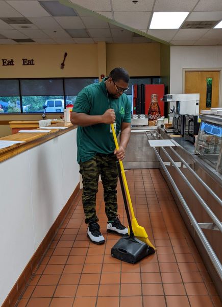Man in green shirt sweeping a cafeteria